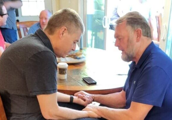 image of two men, Ken Janke and John Spencer, praying at tabl