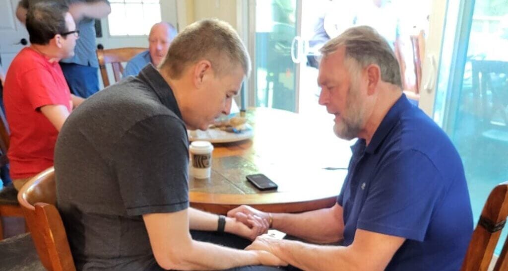 image of two men, Ken Janke and John Spencer, praying at tabl